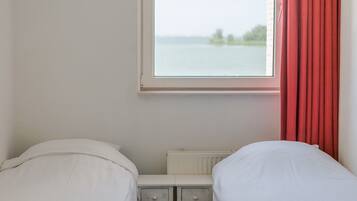 Una habitación con dos camas, una ventana que da a una masa de agua y un radiador debajo de la ventana.