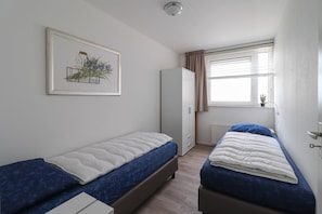 Un dormitorio con dos camas individuales, un armario, un radiador y una ventana con cortinas.