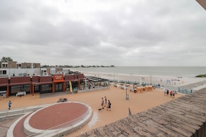 Ett område vid stranden med en löparbana, en byggnad med skylten ”STRAND HUYS”, och en sandstrand.