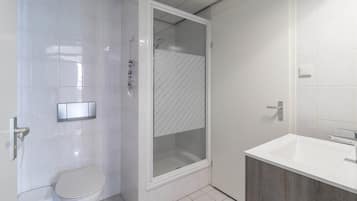A bathroom with a toilet, a shower enclosure, and a sink.