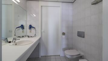 A bathroom with a white sink, two hair dryers, a toilet, and a paper towel dispenser.