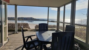 A covered patio with a table and chairs, large windows offering a view of the sea and distant buildings. - Lakeview Suite with Whirlpool in Makkum (Makkum)