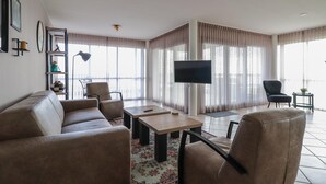 A living room with a sofa, chairs, a coffee table, a TV, and a large window with curtains. - Lakeview Suite with Whirlpool in Makkum (Makkum)