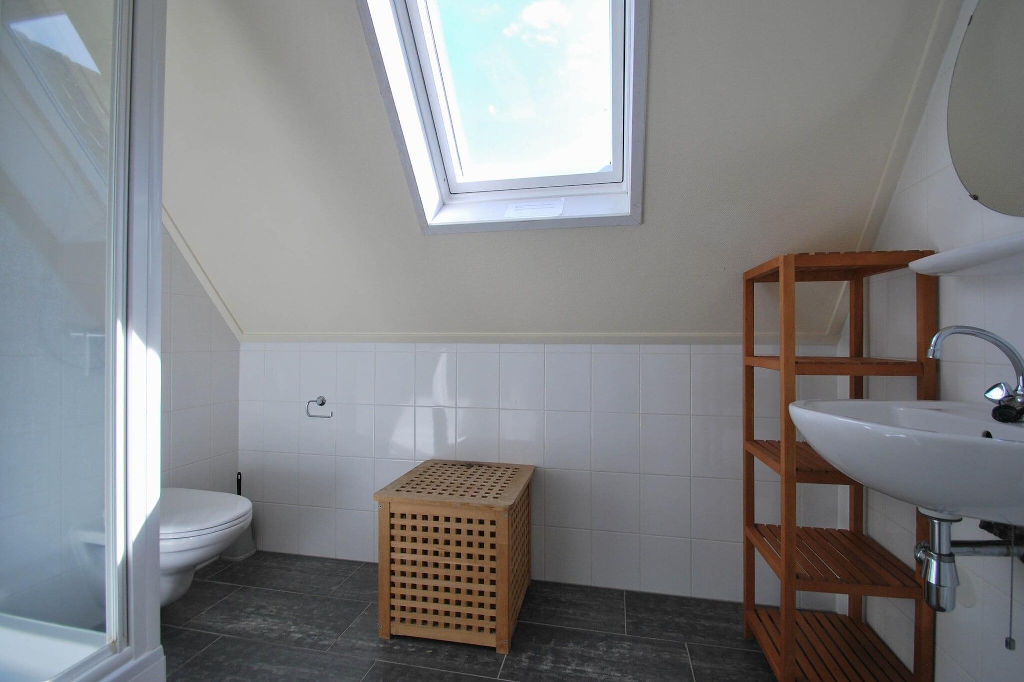 A bathroom with a toilet, a wooden crate, a wooden shelf, and a window.