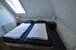 A small room with two beds, a skylight, a radiator, and a nightstand with a lamp. - Classic Beach Villa with Whirlpool (Makkum)