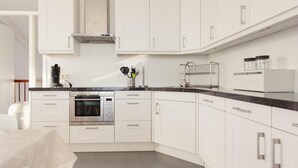 Una cocina moderna con gabinetes blancos, horno empotrado y campana extractora de acero inoxidable.