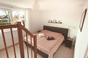 Un dormitorio con cama, mesita de noche, lámpara de noche, ventana y vista al exterior.