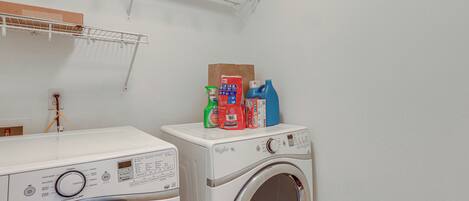 A laundry area with two washing machines, a shelf with cleaning supplies, and a wall-mounted shelf.