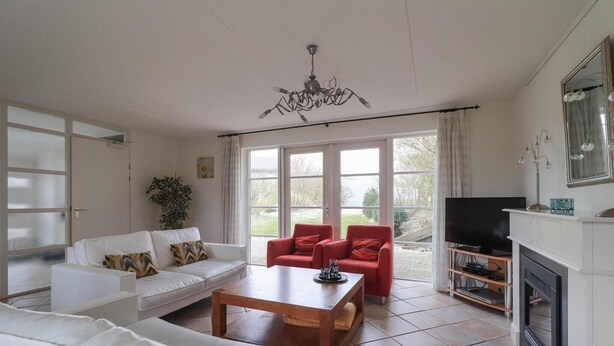 A living room with a white sofa, red chairs, a wooden coffee table, a TV, and a fireplace. - Attractive Dune Villa with Sauna (Makkum)