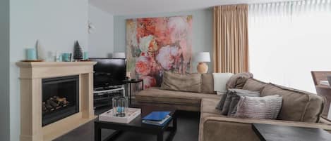 A living room with a fireplace, a television, a sofa, a coffee table, and a large floral painting.
