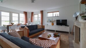 A modern living room with a sofa set, a coffee table, a television, and a fireplace. - Attractive Dune Villa with Sauna (Makkum)