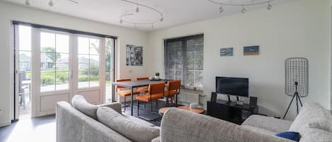 A modern living room with a sofa, dining table, chairs, a TV, and a floor lamp.