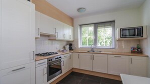 Eine kleine Küche mit weißen Schränken, einem Gasherd, einem Backofen, einer Mikrowelle und einem Fenster mit Jalousien.