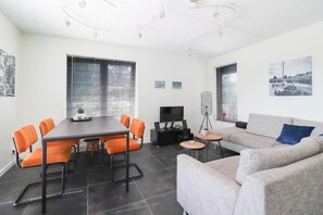 A modern living room with a dining area, a sofa, a TV, and artwork on the walls. - Waterfront Beach Villa for 5 (Makkum)