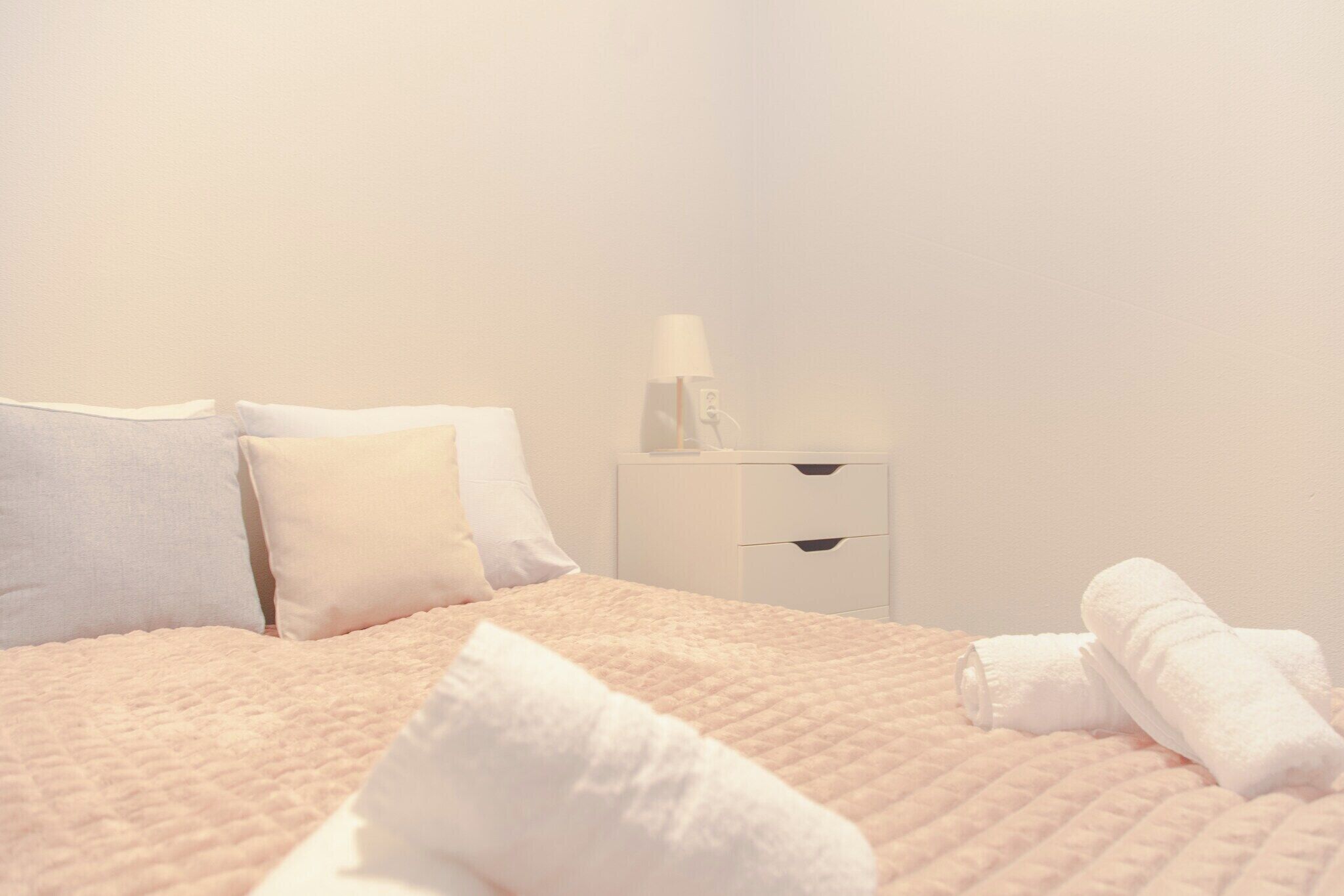 Ein Bett mit gesteppter Decke, weißen Kissen, einem Nachttisch mit Lampe und aufgerollten Handtüchern.