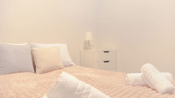 Ein Bett mit gesteppter Decke, weißen Kissen, einem Nachttisch mit Lampe und aufgerollten Handtüchern.