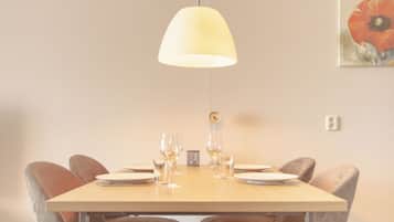 A dining area with a table set for four, a hanging light fixture, and a clock on the wall.