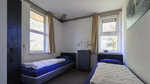 Eine kleine Unterkunft mit einem Schlafzimmer, zwei Betten, einem Schreibtisch und einem Fenster.