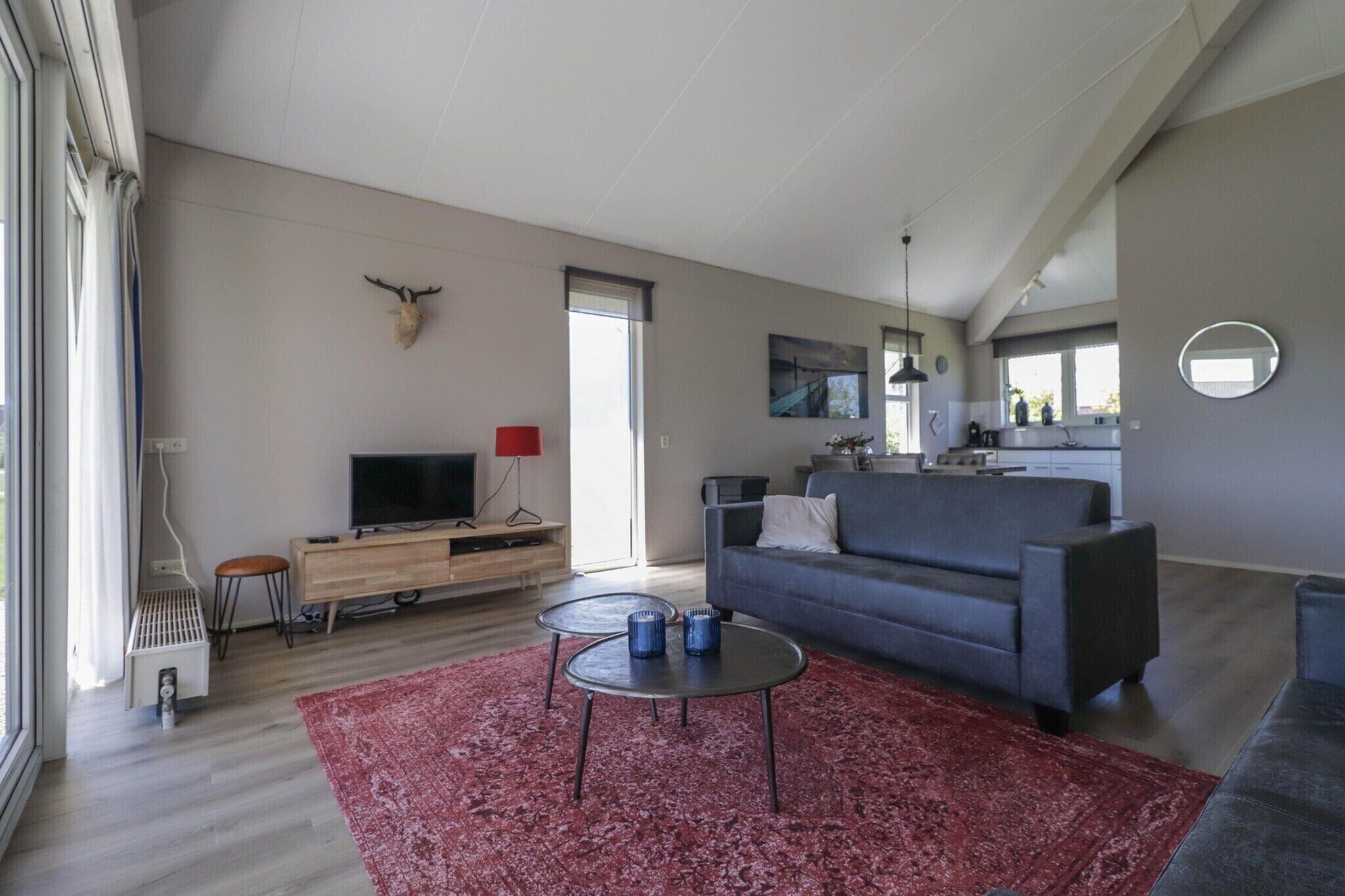 Ein modernes Wohnzimmer mit einer Couch, einem Fernseher, einem roten Teppich und einer Küche im Hintergrund.