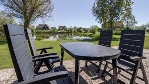 Ein Sitzbereich im Freien mit Tisch und Stühlen, einem Teich und Häusern im Hintergrund.