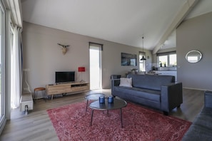 A modern living room with a sofa, a TV, a fireplace, and a dining area. - Compact Waterfront Wellness Bungalow (Makkum)