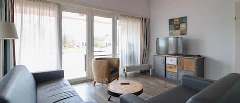 Ein modernes Wohnzimmer mit einer Couch, einem runden Couchtisch, einem Korbstuhl, einem Fernseher und einem Schrank.