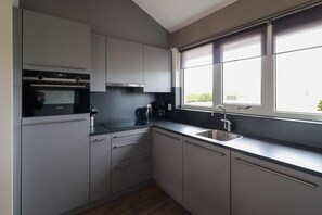 Eine moderne Küche mit weißen Schränken, einem Einbauofen, einer Kaffeemaschine und einem Fenster für natürliches Licht.