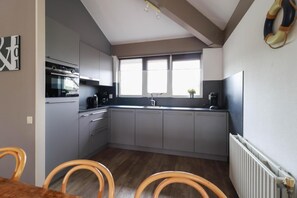 Eine kompakte Küche mit grauen Schränken, einem eingebauten Backofen und einem Fenster über der Spüle.