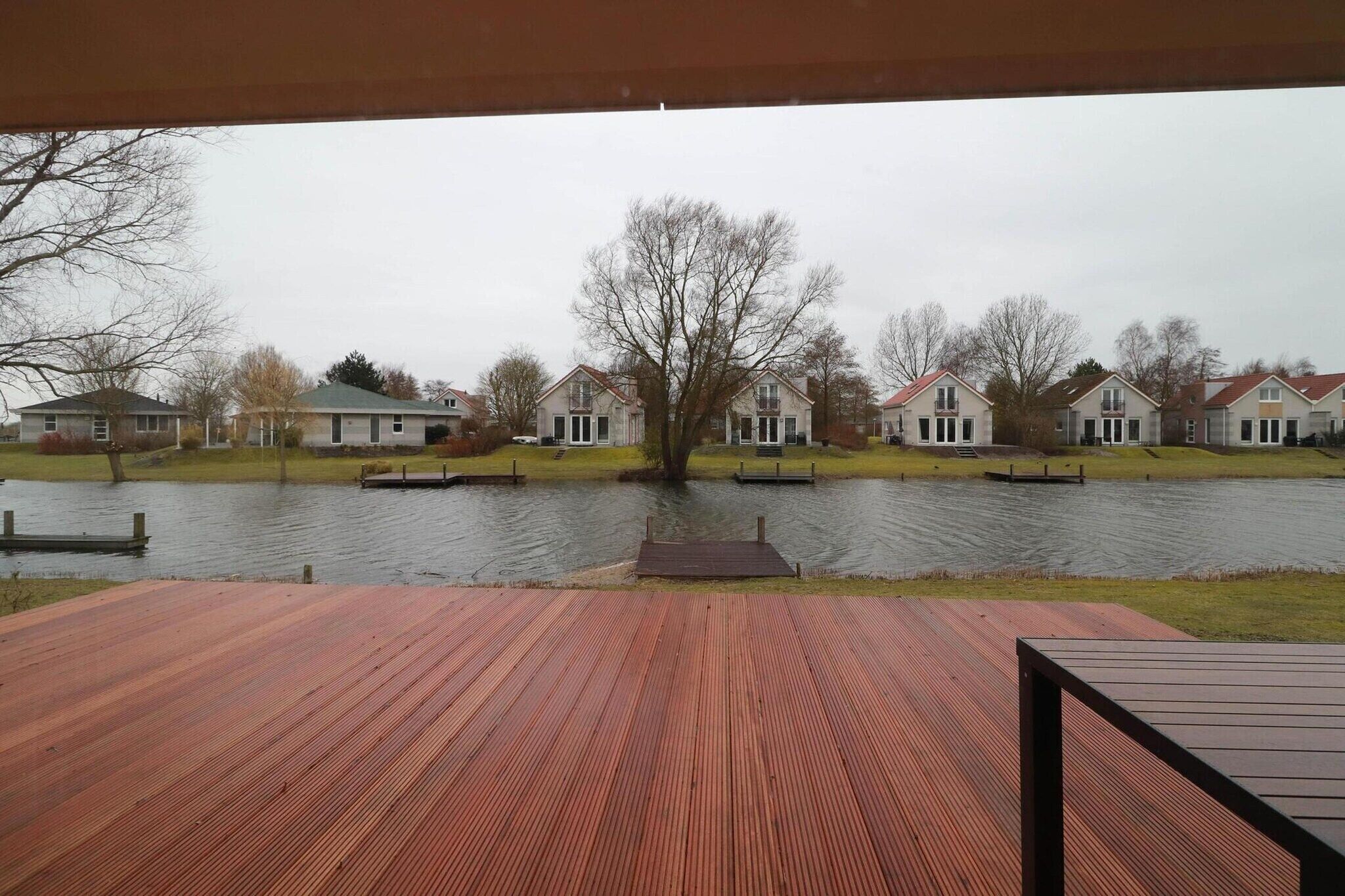 A waterfront property with a wooden deck, a dock, and a row of houses across the water.