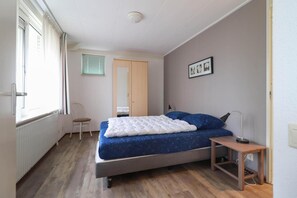 Ein Schlafzimmer mit Bett, Stuhl, Nachttisch, Fenster und Tür.