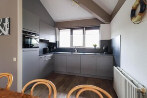 A compact kitchen with grey cabinets, a built-in oven, a sink, and a window above the countertop.
