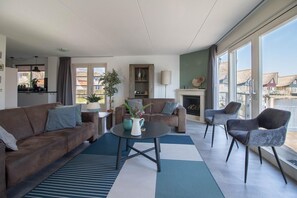 A modern living room with a sofa, armchairs, a coffee table, a fireplace, and large windows offering a view of the city. - Luxury Waterfront Wellness Villa (Makkum)