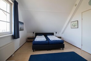 A bedroom with a sloped ceiling, a bed with two pillows, a bedside table, a radiator, and a window with curtains. - Luxury Waterfront Wellness Villa (Makkum)