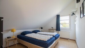 Ett sovrum med en säng, sängbord, en lampa, ett fönster med gardiner och ett element.
