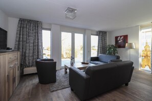Ein modernes Wohnzimmer mit einer Couch, einem Couchtisch, einem Fernseher und einem großen Fenster mit Vorhängen.
