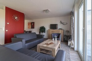 Ein Wohnzimmer mit einer Sofagarnitur, einem Couchtisch, einem Fernseher und einem Fenster mit Blick.