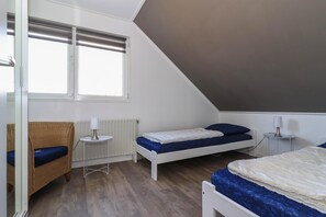 Ein Zimmer mit zwei Betten, einem Sessel, einem kleinen Tisch und einem Fenster.
