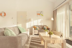 Ein modernes Wohnzimmer mit einer Couch, einem Couchtisch und einem Beistelltisch. Eine Tür mit einem Schild, eine Lampe und ein Fenster mit Vorhängen sind ebenfalls zu sehen.