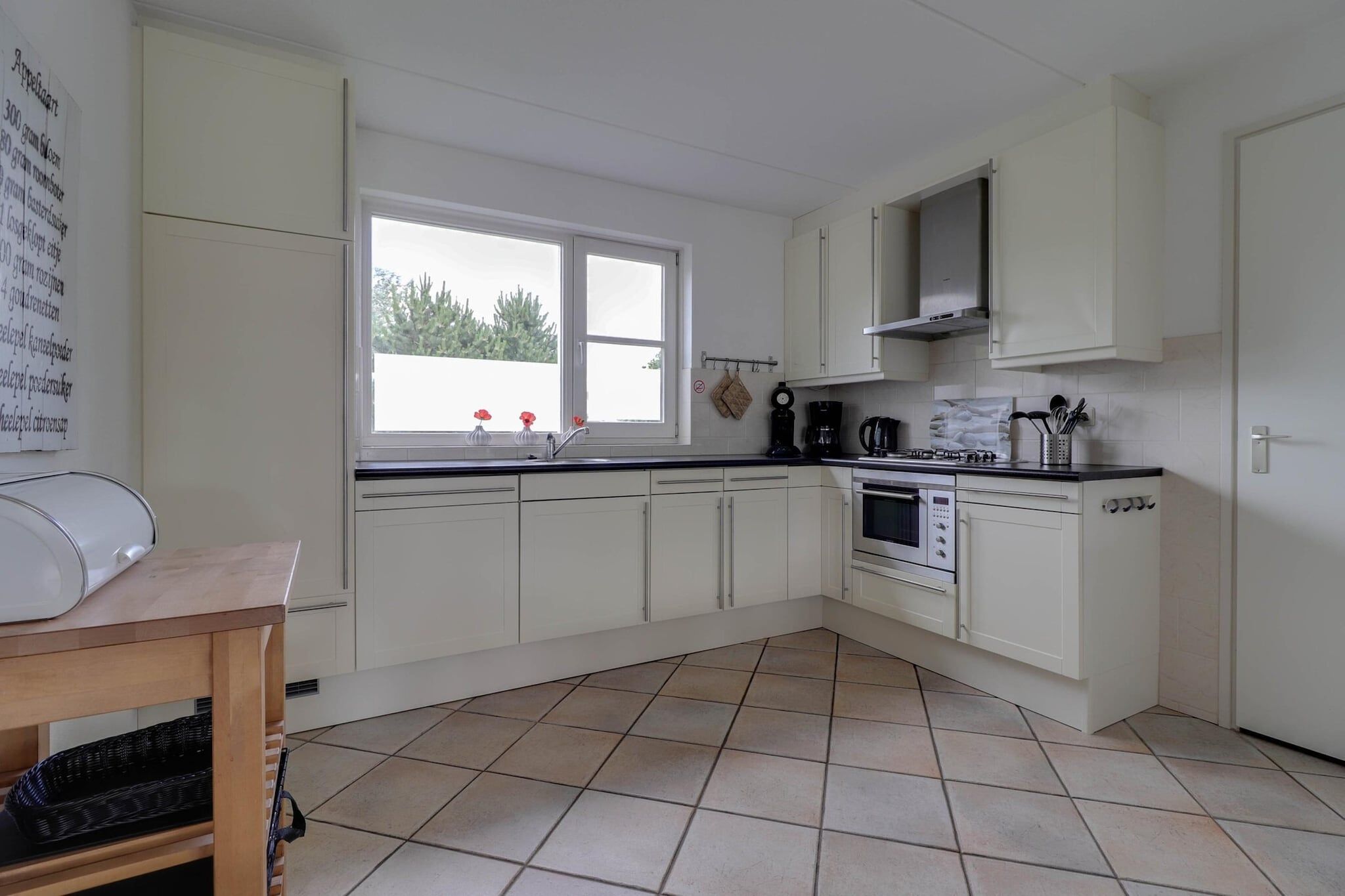 A kitchen with white cabinets, a stove, oven, and a window with a view of greenery.