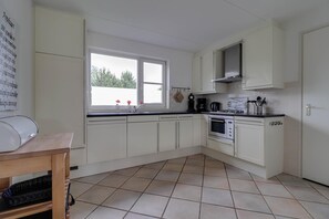 Een keuken met witte kastjes, een fornuis, oven en een raam met uitzicht op groen.