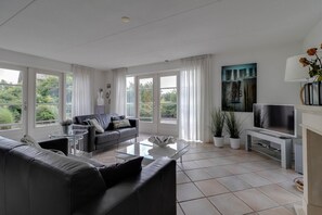 Ein modernes Wohnzimmer mit Sofa, Couchtisch, Fernseher und großen Fenstern.