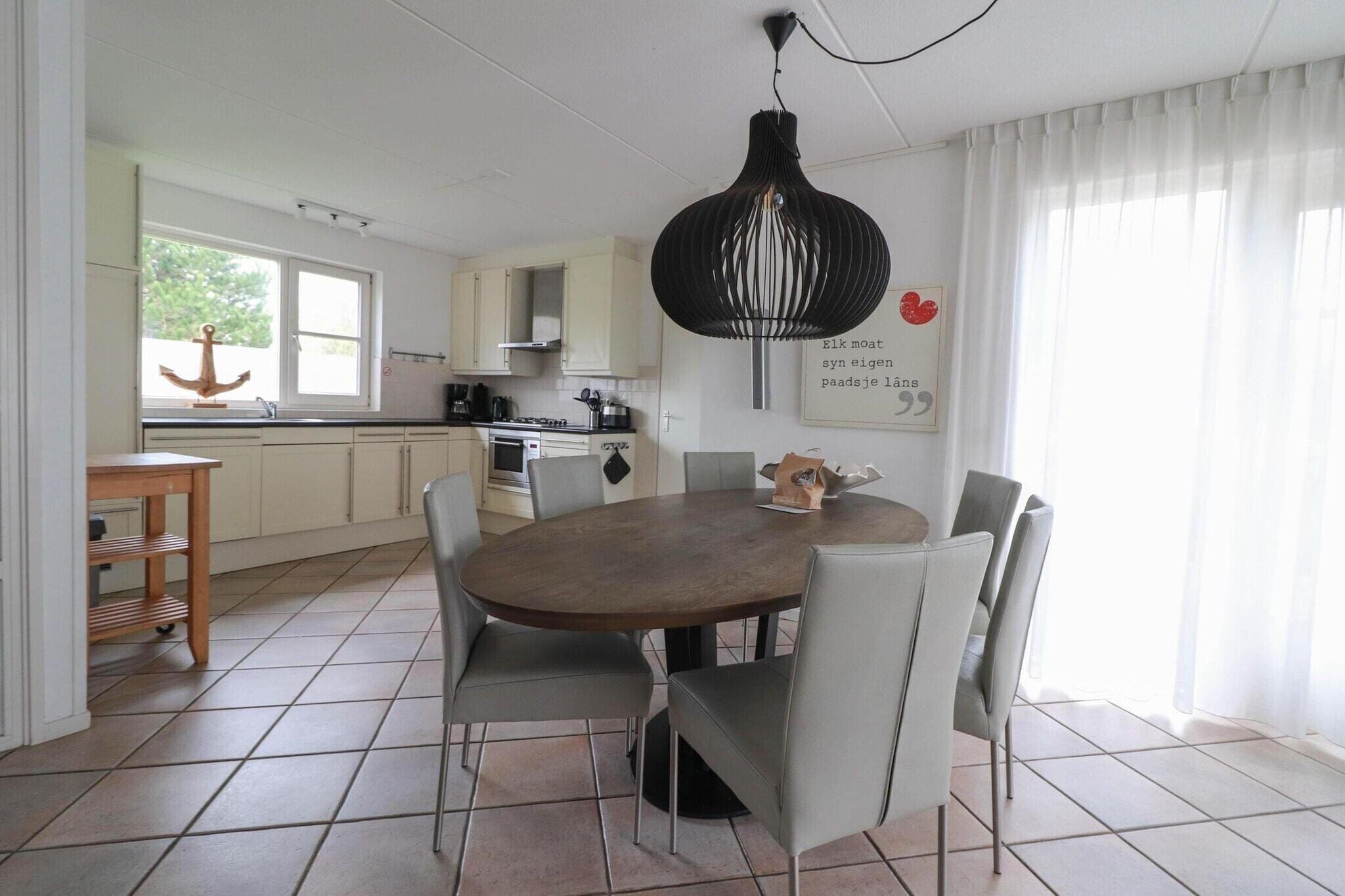 A modern kitchen with a round dining table and chairs, a pendant light, and a window with curtains.