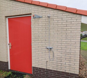 Eine rote Tür, eine Ziegelwand und ein an der Wand befestigter Metallschlauch.
