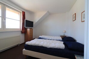 A bedroom with a bed, a television, a window with curtains, and a radiator. - Beachside Dune Villa with Garden (Makkum)