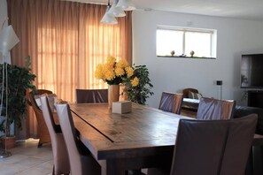 A dining area with a wooden table, chairs, a vase of yellow flowers, and a television on the wall. - Beachside Dune Villa with Garden (Makkum)