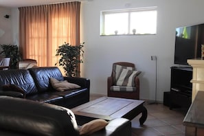 Ein Wohnzimmer mit einem schwarzen Ledersofa, einem Holztisch, einem gemusterten Sessel und einem Fernseher auf einem Schrank.