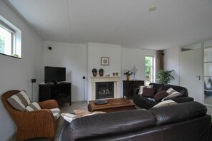 A living room with a fireplace, a television, and seating arrangements. - Beachside Dune Villa with Garden (Makkum)