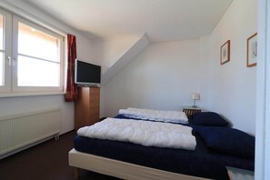Een slaapkamer met een bed, een televisie, een raam met gordijnen en een radiator.