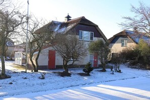 Een woonhuis met een rode deur, schoorsteen en een sneeuwbedekte voortuin.