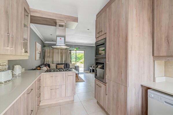 A modern kitchen with wooden cabinets, a central island, built-in oven, and a dishwasher.